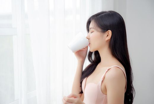 Beautiful young asian sexy woman in underwear drinking coffee near windows in the morning, girl with seductive figure fit drinking beverage for relax and resting after wake up, lifestyle concept.