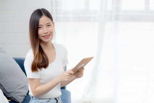 Young attractive asian woman resting using browsing tablet computer on sofa at home, happy girl sitting on couch relax reading digital gadget at house, communication and lifestyle concept.