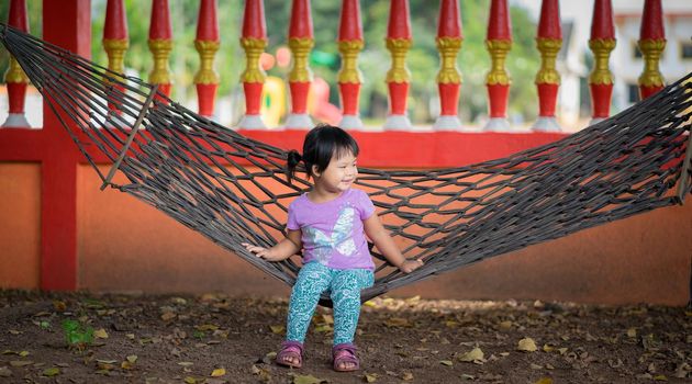 little asian girl in violet shirt sitting on cradle