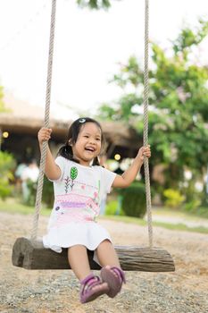 Little girl in white dress sitting on a swing in the park