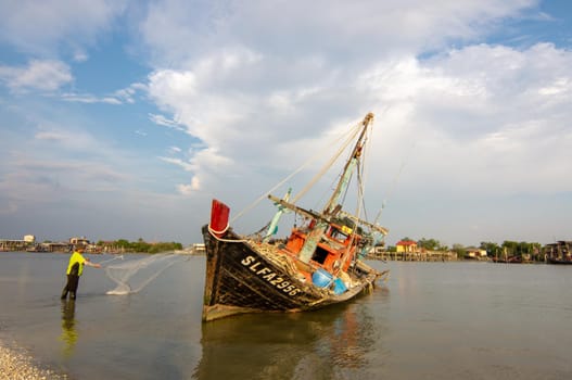 Sekinchan, Selangor/Malaysia - Oct 06 2019: A fisherman cast the net beside fishing boat.