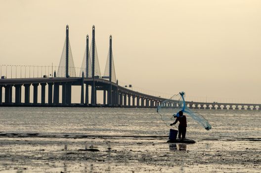 George Town, Penang/Malaysia - Dec 28 2019: Fisherman cast net. Background is Penang Second Bridge.