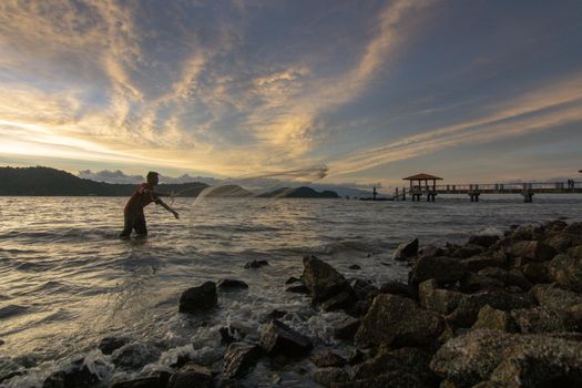 Batu Kawan, Penang/Malaysia - Mar 21 2017: Fisherman cast net near rock coastal in sunset hour.