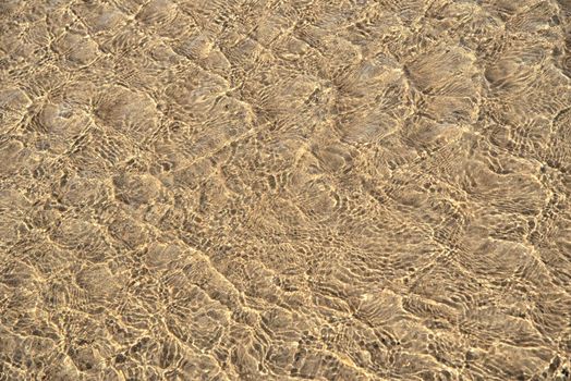 Surface of sea water with ripples on beach sand. Water surface background, texture.