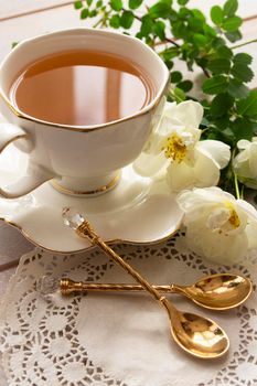 Gorgeous bouquet of fresh roses in old antique faience, ceramic, porcelain pitcher with golden on round aged plate, china tea cup with golden spoons. Vertical image