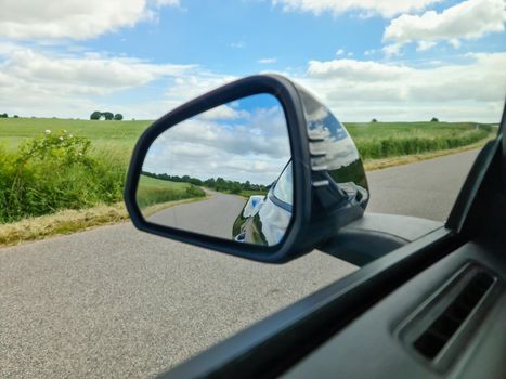 View into the side mirror of a black sports car while driving