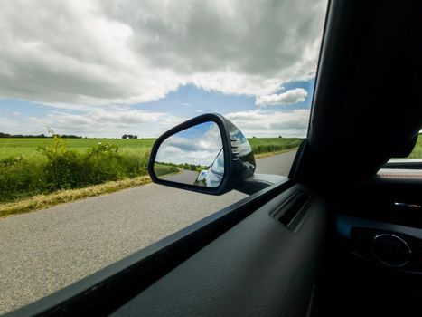 View into the side mirror of a black sports car while driving