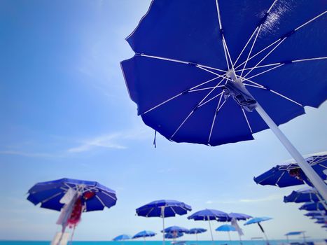 blue sun umbrellas open and arranged in rows at an Italian beach on a sunny summer day. Beach holidays in the summer and relaxation.