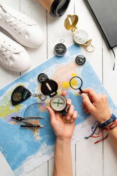 Top view woman planning a trip, holding compass and magnifying glass, looking at map. Flat lay