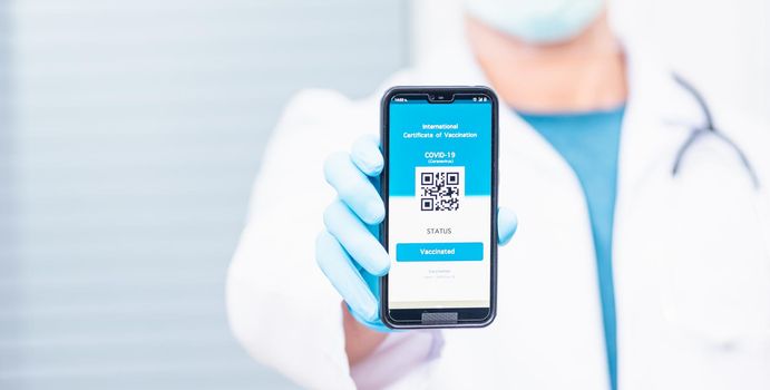 Doctor man in medical mask show app smartphone mobile digital vaccinated passport coronavirus (COVID-19) certificate to confirm, vaccine health pass concept