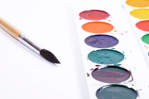 Colorful watercolor palette, top view of paintbrushes palette with brush on white paper background