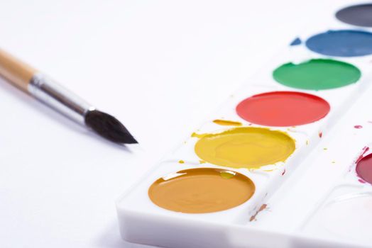 Colorful watercolor palette, top view of paintbrushes palette with brush on white paper background