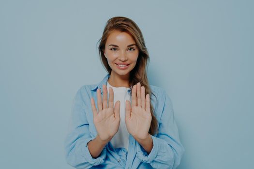 Young beautiful woman in casual clothes standing and holding both hands out in stop gesture isolated on blue background with copy space. Body language. Non-verbal communication. Prevent problem