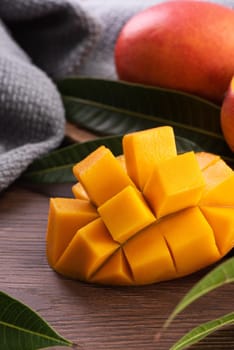 Mango. Close up of fresh ripe mango fruit with leaves over dark wooden table background with green leaves.