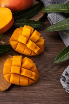 Mango. Close up of fresh ripe mango fruit with leaves over dark wooden table background with green leaves.