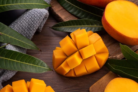 Mango. Close up of fresh ripe mango fruit with leaves over dark wooden table background with green leaves.