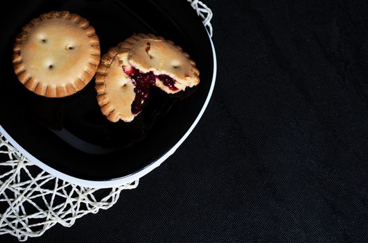 Cookies with jam on black plate on black backgroung up view