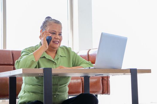 Asian women Retirement Use a smartphone and laptop in the living room concept to work at home. Quarantine to prevent spreading disease Or a conversation with someone far away Via the Internet