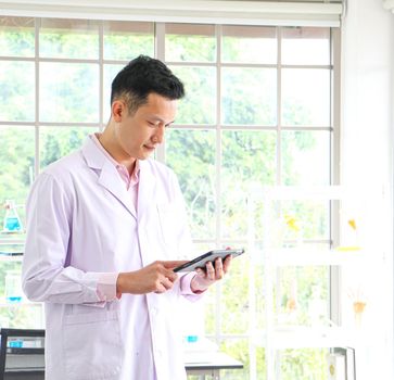 An Asian scientist or researcher wearing white clothes. He carried a tablet with a science lab and Laboratory test tubes during working hours In the concept of corona vaccine research and development