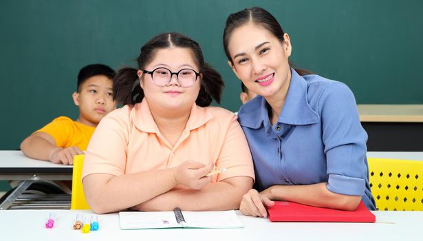 Asian disabled children Or, an autistic child learns to read, write, and train their hand and finger muscles with a teacher at their classroom desk. Concentrate and smile Happy disability kid concept