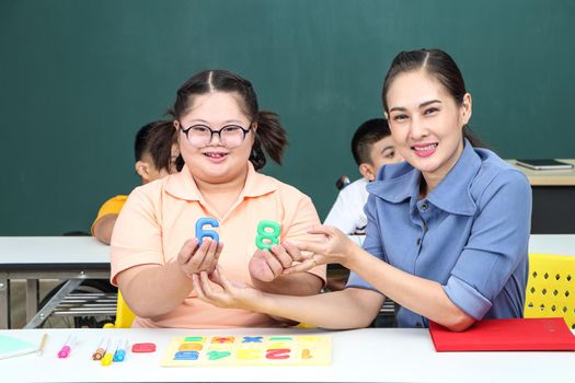 Asian disabled children Or, an autistic child learns to read, write, and train their hand and finger muscles with a teacher at their classroom desk. Concentrate and smile Happy disability kid concept