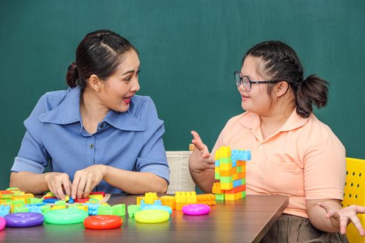 An Asian girl with a disability is practicing the use of hand and finger muscles. By playing with toys With a helping teacher to care for happiness and concentration in the classroom