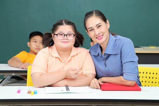 Asian disabled children Or, an autistic child learns to read, write, and train their hand and finger muscles with a teacher at their classroom desk. Concentrate and smile Happy disability kid concept