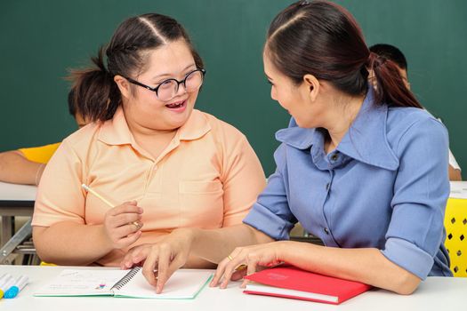 Asian disabled children Or, an autistic child learns to read, write, and train their hand and finger muscles with a teacher at their classroom desk. Concentrate and smile Happy disability kid concept