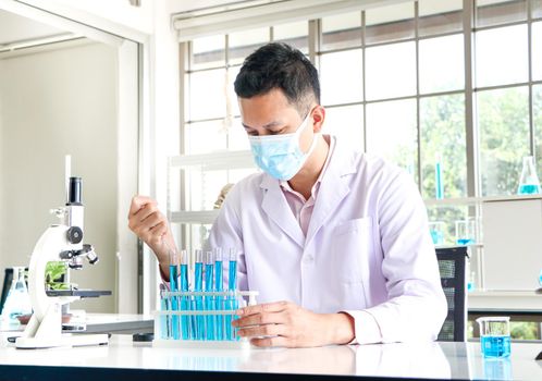 An Asian scientist or chemist drops a blue liquid chemical in a laboratory. Research concepts in healthcare, pharmacy, and medicine. Liquid analysis to separate DNA and molecules in vitro.