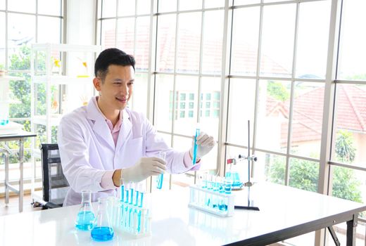 An Asian scientist or chemist drops a blue liquid chemical in a laboratory. Research concepts in healthcare, pharmacy, and medicine. Liquid analysis to separate DNA and molecules in vitro.