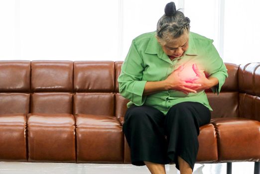Asian elderly woman Grasping the chest in pain while sitting on the sofa inside the room Health care concept Women suffering from chest pain Senior female health problems heart and people's concept