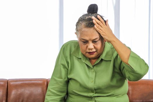 Asian elderly woman Grasping the head in pain while sitting on the sofa in the room Health care concept Women suffering from headaches Senior female health problems and people's concepts