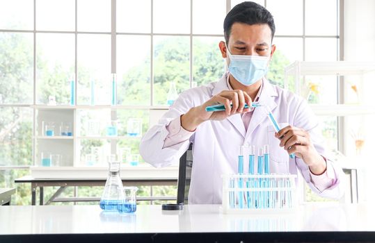 An Asian scientist or chemist drops a blue liquid chemical in a laboratory. Research concepts in healthcare, pharmacy, and medicine. Liquid analysis to separate DNA and molecules in vitro.