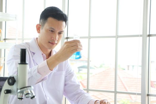 Asian scientist or chemist looks at a blue liquid chemical test tube in the laboratory. Research concepts in healthcare, pharmacy, and medicine. Liquid analysis to separate DNA and molecules in vitro.