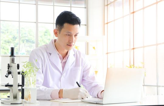 Asian researchers in white coats Work in a scientific laboratory use a laptop to find information And write down the test results in a notebook or make a report in a scientific laboratory