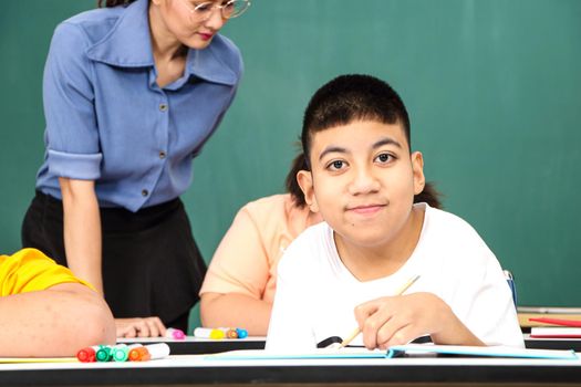 Asian disabled children Or, an autistic child learns to read, write, and train their hand and finger muscles with a teacher at their classroom desk. Concentrate and smile Happy disability kid concept