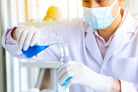 An Asian scientist or chemist drops a blue liquid chemical in a laboratory. Research concepts in healthcare, pharmacy, and medicine. Liquid analysis to separate DNA and molecules in vitro.