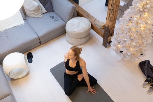 Beautiful blonde woman doing home workout indoors. Woman practice yoga at home. Fit girl using workout tutorials for healthy active lifestyle. Woman using quarantine for home workouts and stretching