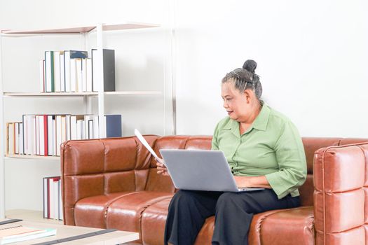 Asian women Retirement Use a smartphone and laptop in the living room concept to work at home. Quarantine to prevent spreading disease Or a conversation with someone far away Via the Internet