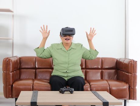 Retired Asian women are enjoying VR  glasses for advanced augmented reality headsets in an amazing 3D format on the couch, the concept of technological innovation, and relaxing fun. For adults at home