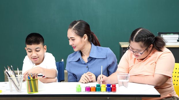 A handicapped Asian girl is practicing hand and finger muscles by drawing and painting with water. With a helping teacher to care for happiness and concentration in the classroom