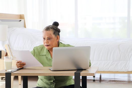 Senior Asian women Carrying documents with a laptop A concept that manages home utility bills or money for older women who use their computers to work or work documents online. Aging and technology