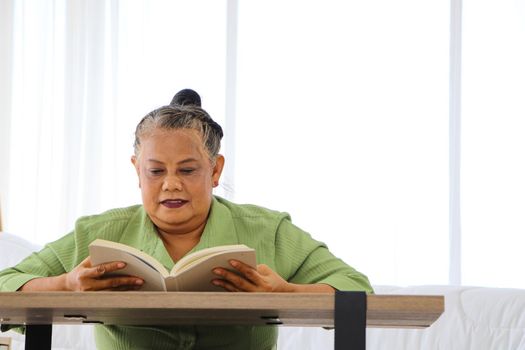 Senior Asian women Retirement Asians Sit and read movies and media at the wooden table in the bedroom. The concept of a relaxed retirement life Enjoy happy