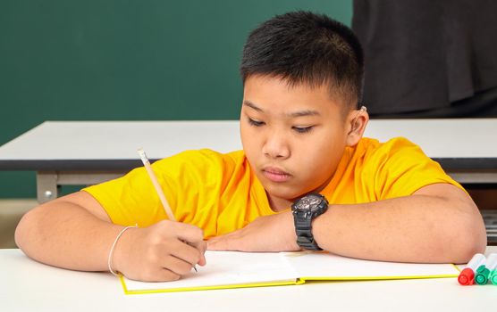 Asian disabled boy Or an autistic child in yellow shirts holding a pencil to learn to read and write at the classroom desk with concentration.