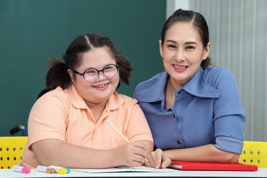 Asian disabled children Or, an autistic child learns to read, write, and train their hand and finger muscles with a teacher at their classroom desk. Concentrate and smile Happy disability kid concept