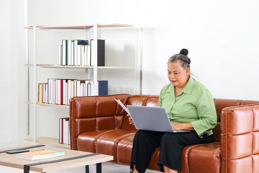 Asian women Retirement Use a smartphone and laptop in the living room concept to work at home. Quarantine to prevent spreading disease Or a conversation with someone far away Via the Internet