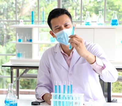 Asian scientist or chemist looks at a blue liquid chemical test tube in the laboratory. Research concepts in healthcare, pharmacy, and medicine. Liquid analysis to separate DNA and molecules in vitro.