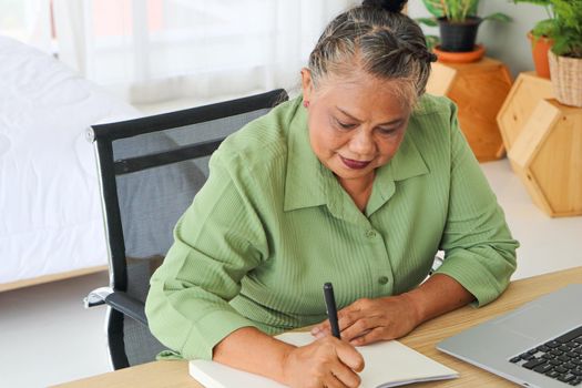 Senior woman retiring Asian Work, write and use the computer at the desk in the relaxing room. And working at the home of retirement