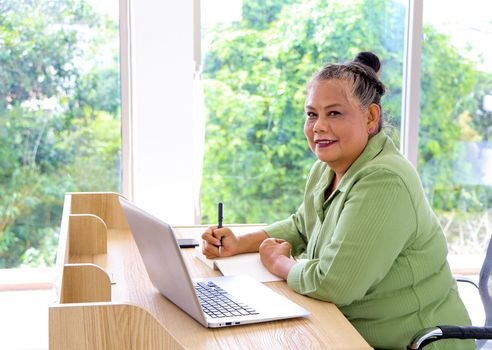 Senior woman retiring Asian Work, write and use the computer at the desk in the relaxing room. And working at the home of retirement