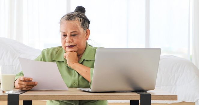 Senior Asian women Carrying documents with a laptop A concept that manages home utility bills or money for older women who use their computers to work or work documents online. Aging and technology